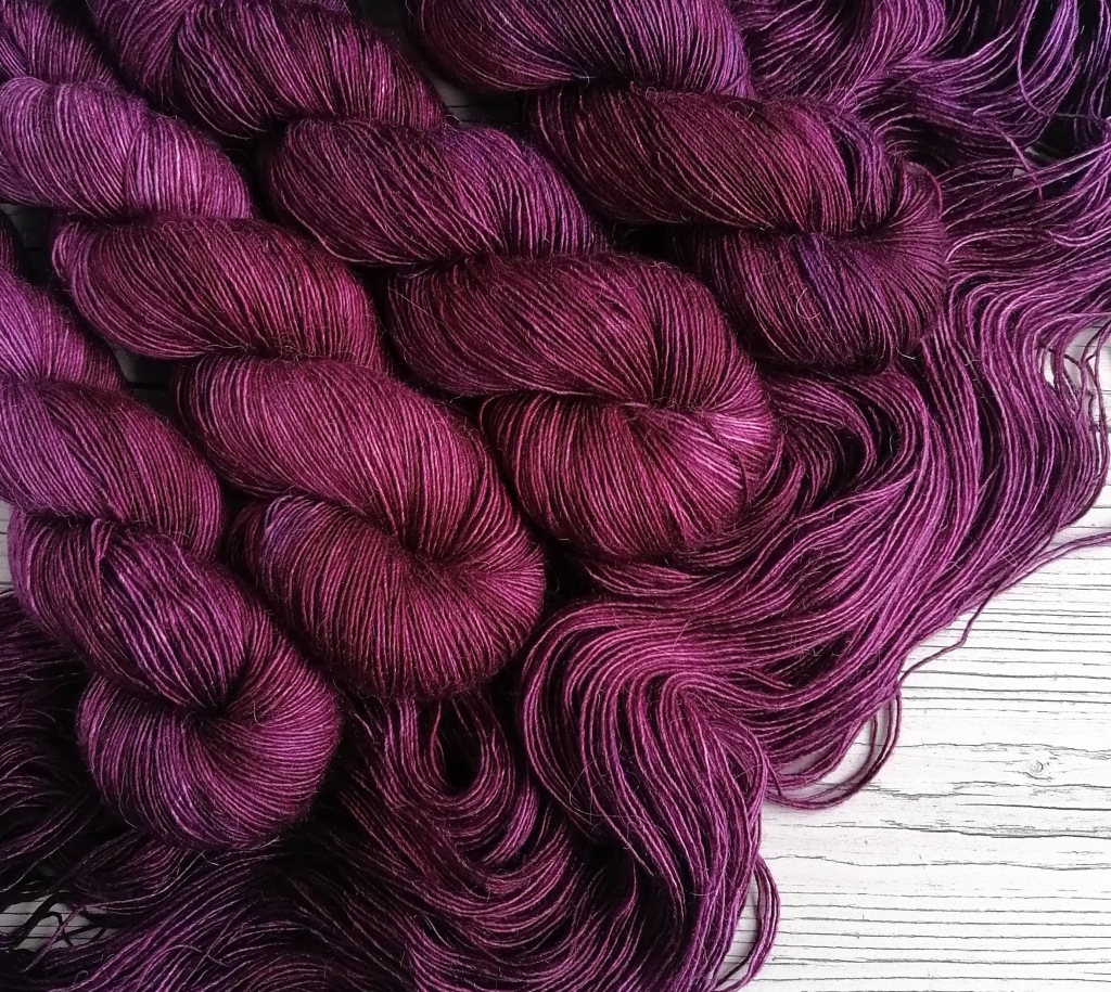 several skeins of yarn in a shade of deep plum purple laid flat on a wooden surface