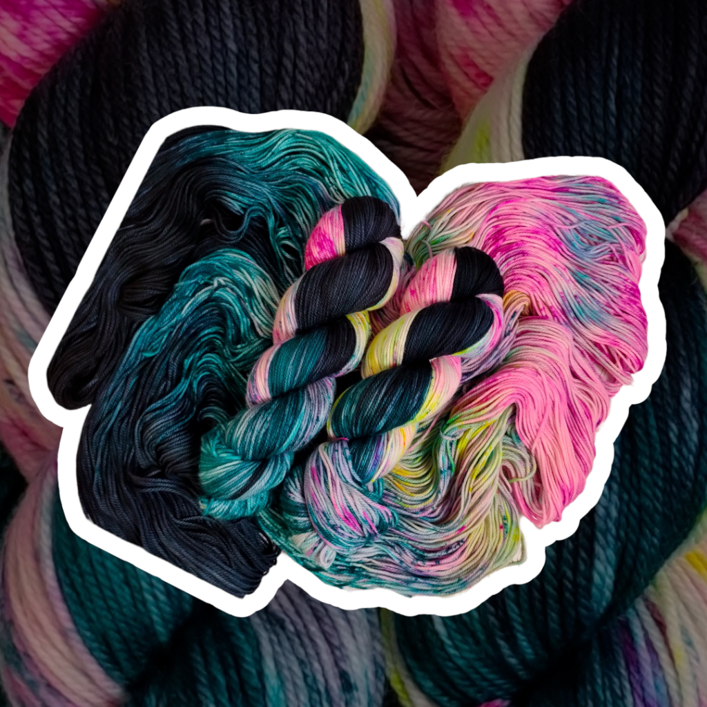two skeins of yarn in shades of black, blue and pink arranged in front of a background of the same skeins