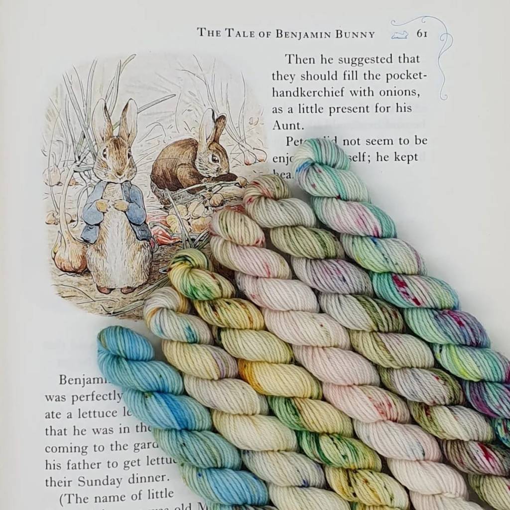 6 mini skeins of yarn in pastel colours inspired by The Tale of Benjamin Bunny sitting on top of the book 