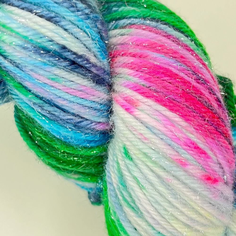 a close up of a skein of sparkly yarn in shades of green pink and blue 