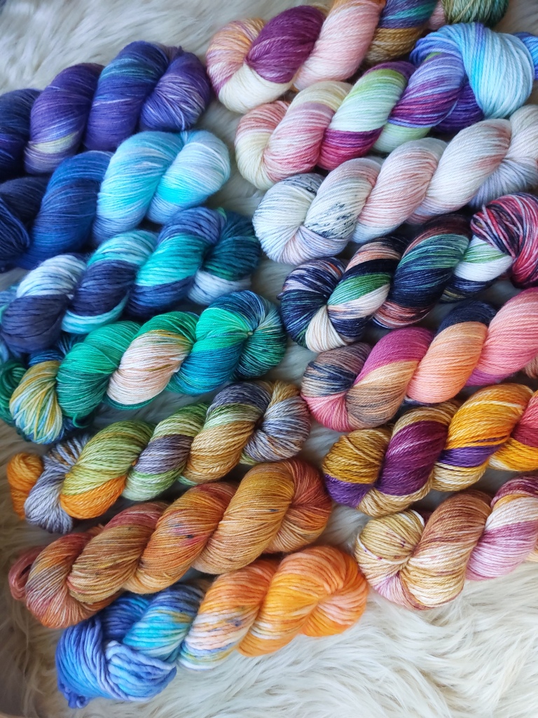 several skeins of yarn laid in 2 rows, with blues and purples at the top ranging down to oranges and browns at the bottom 