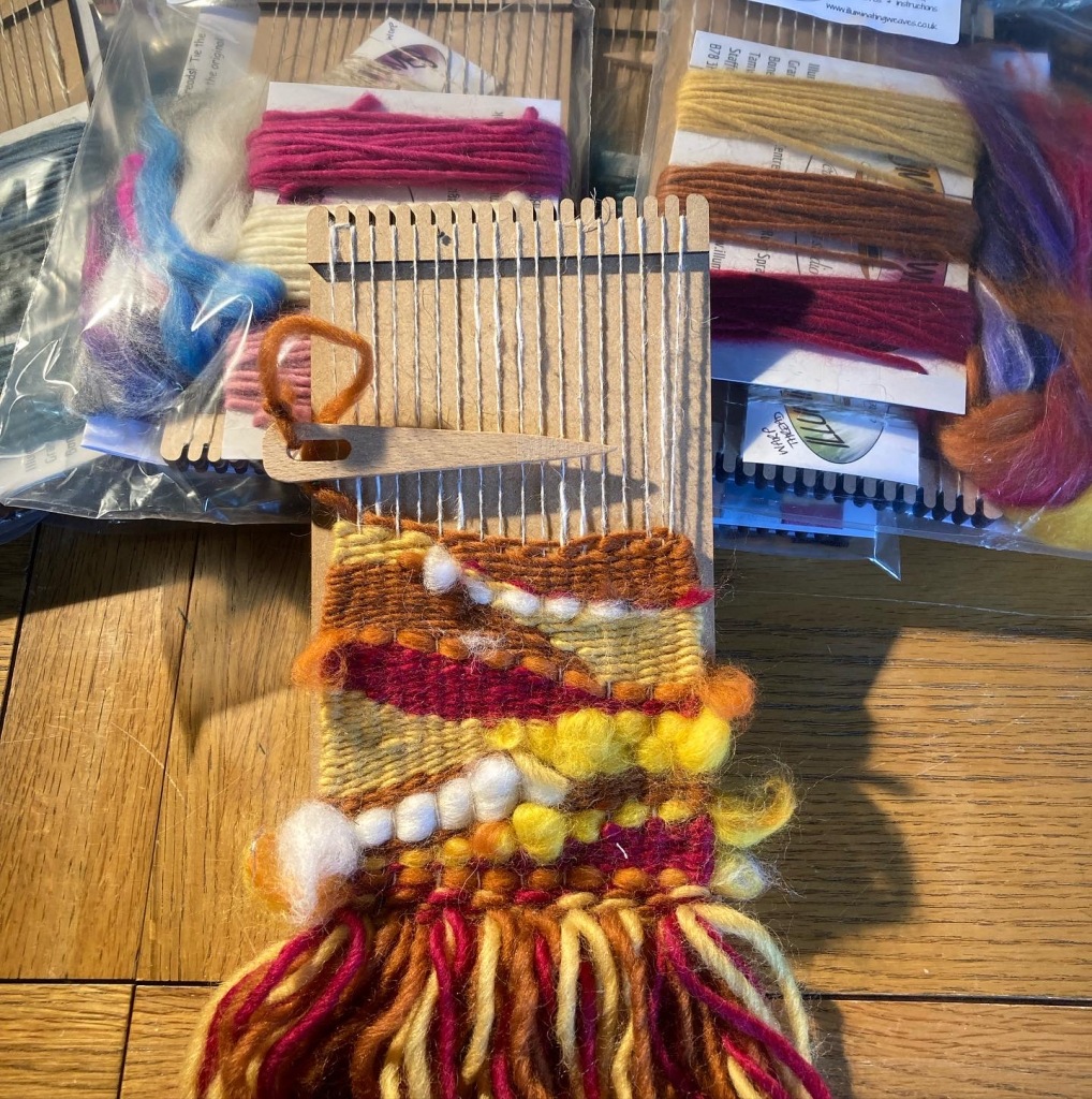 a picture of some weaving kits with a small piece of art weaving in progress in the foreground 