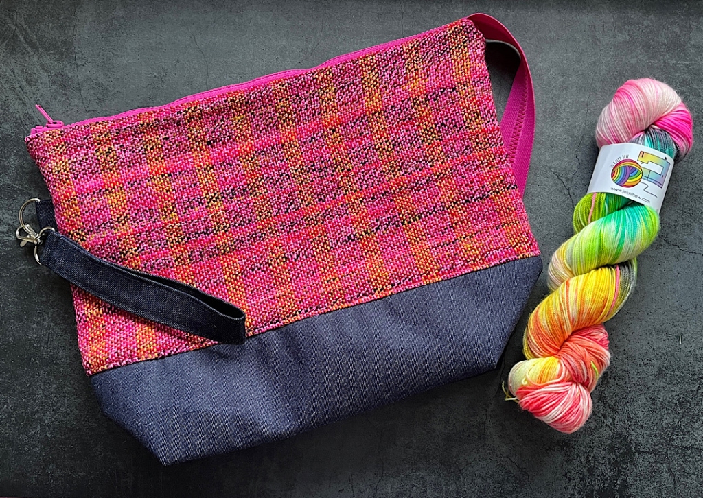 a woven project bag in shades of pink and orange with a skein of hand-dyed 4 ply yarn alongside it 