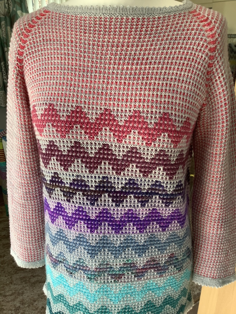 a hand knitted sweater with the main body in shades of pink and cream and then a diagonal pattern on the lower half in shades of pink, purple and blue 