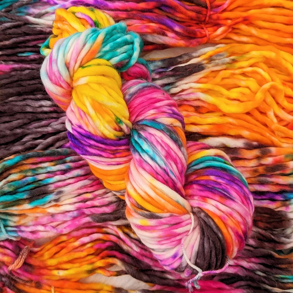 a bright skein of hand-dyed chunky yarn in shades of pink, yellow, purple and blue 