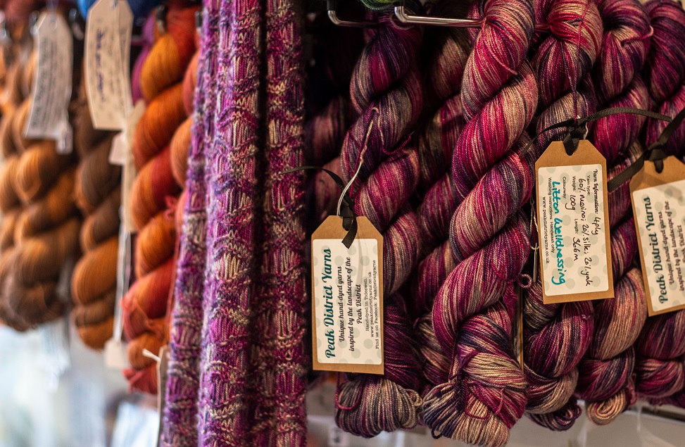 several skeins of yarn in shades of pink, orange and brown on hooks