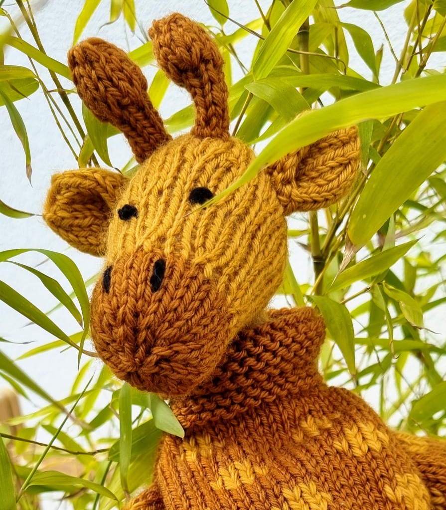 a knitted giraffe pokes through a houseplant