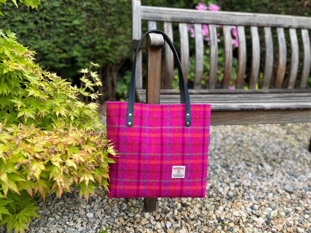 a bright pink tweed bag hangs off the arm of a park bench