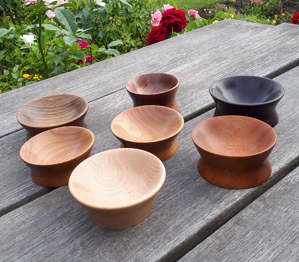several wooden spindle support bowls sit on a wooden table in a garden