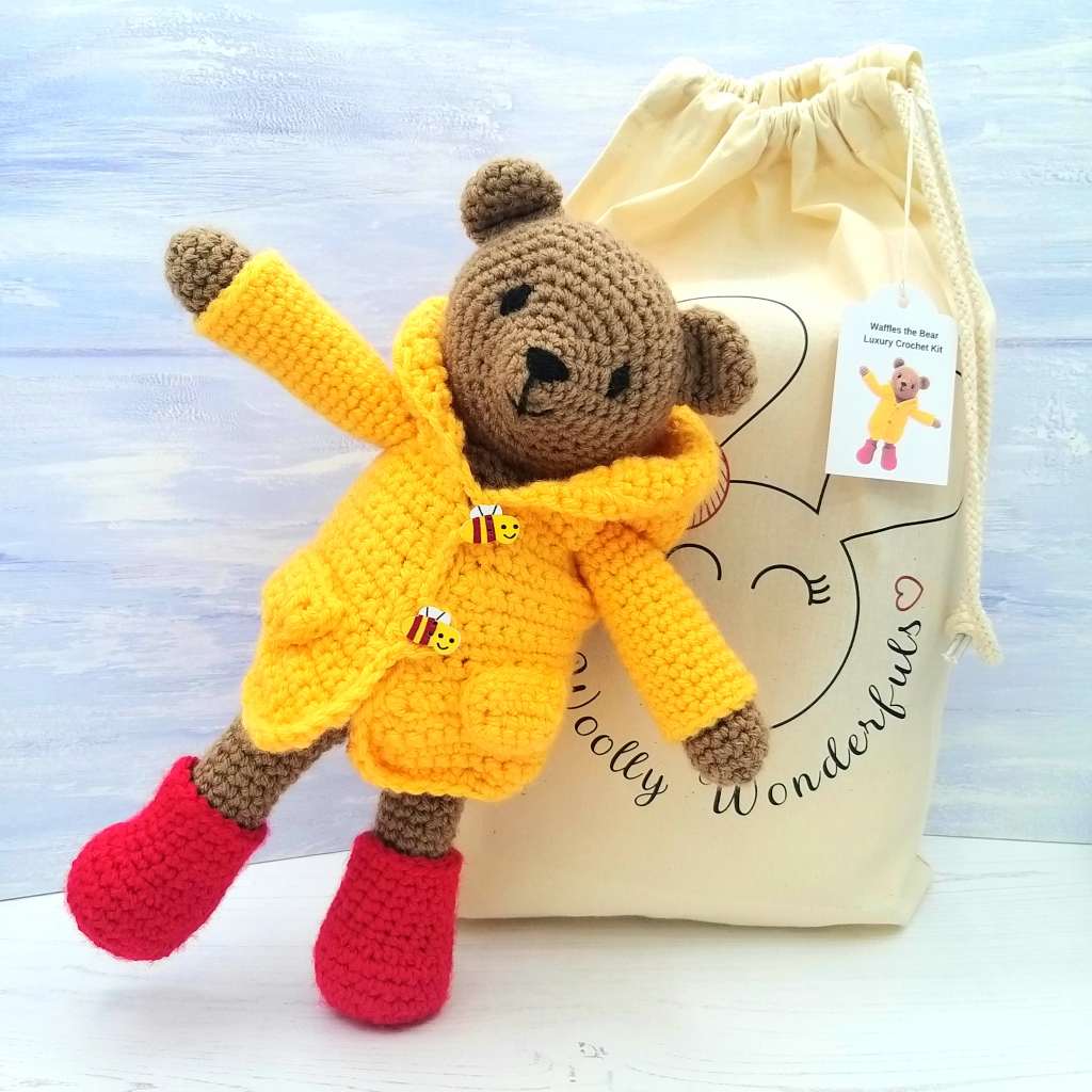 a crocheted toy bear wearing a yellow coat and red boots 